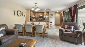 A living room with a dining area, a kitchen in the background, and a balcony with curtains.