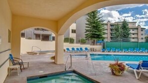 A pool area with a hot tub, lounge chairs, and a view of buildings in the background.