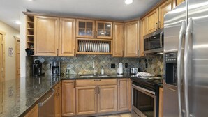 A kitchen with wooden cabinets, a stainless steel refrigerator, a microwave, and a tiled backsplash.