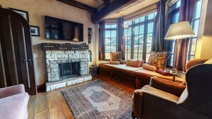 A cozy living room with a stone fireplace, comfortable seating, and large windows offering a view of the outdoors. - Juniper Ridge 16 5000 sq ft, Grand Chateau at Eagle, Expansive Mountain Views by RedAwning (Mammoth Lakes)
