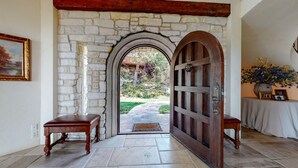 A stone archway leading to a garden, a wooden door with a metal handle, a bench, and a table with a vase of flowers. - Juniper Ridge 16 5000 sq ft, Grand Chateau at Eagle, Expansive Mountain Views by RedAwning (Mammoth Lakes)