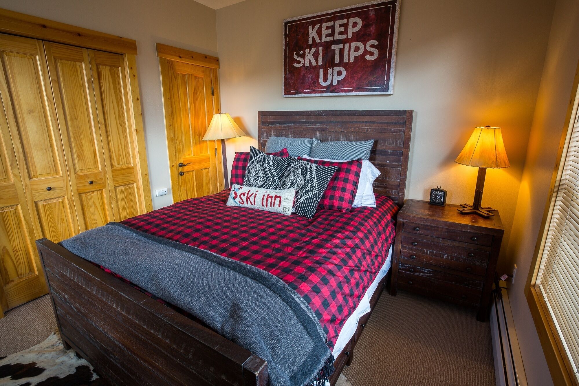 A cozy bedroom with a large bed, wooden wardrobe, and a sign that reads "KEEP SKI TIPS UP".
