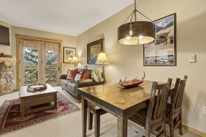 A dining area with a wooden table and chairs, a chandelier, and a view of the outdoors through a window. - Spacious, Mountain Chic, Close to Ski Lift 1 bedroom - TM316 by Redawning (Copper Mountain)