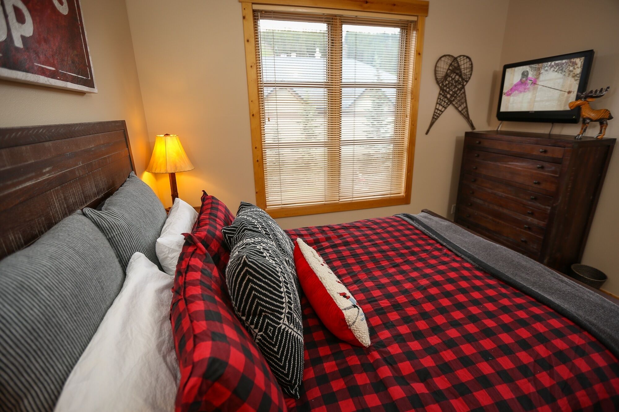 Un dormitorio acogedor con cama, cómoda, lámpara y ventana con persianas.