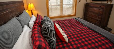 Un dormitorio acogedor con cama, cómoda, lámpara y ventana con persianas.
