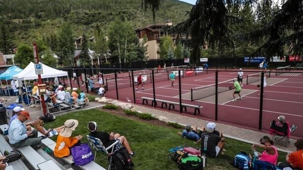 Una cancha de tenis con espectadores sentados en bancos y sillas alrededor.