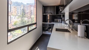 A modern kitchen with a large window, stainless steel appliances, and a view of buildings. - w* | Classy 1BR Penthouse in Cabrera (Bogotá)