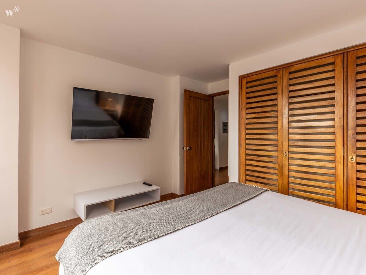 Une chambre à coucher avec un lit, un téléviseur fixé au mur, une armoire en bois et un banc.