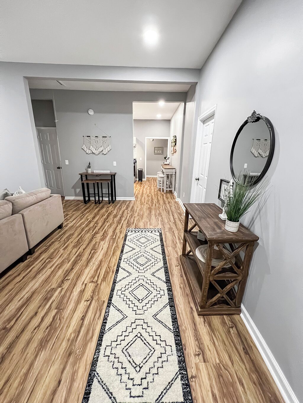 A modern living room with a wooden floor, a beige sofa, a dining table with chairs, and a decorative mirror.