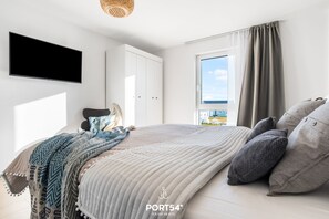 A modern bedroom with a large bed, a wardrobe, a television, and a window with curtains. - StrandLoft - Infrared sauna, fireplace, balcony, beach chair, Baltic Sea view (Olpenitz)
