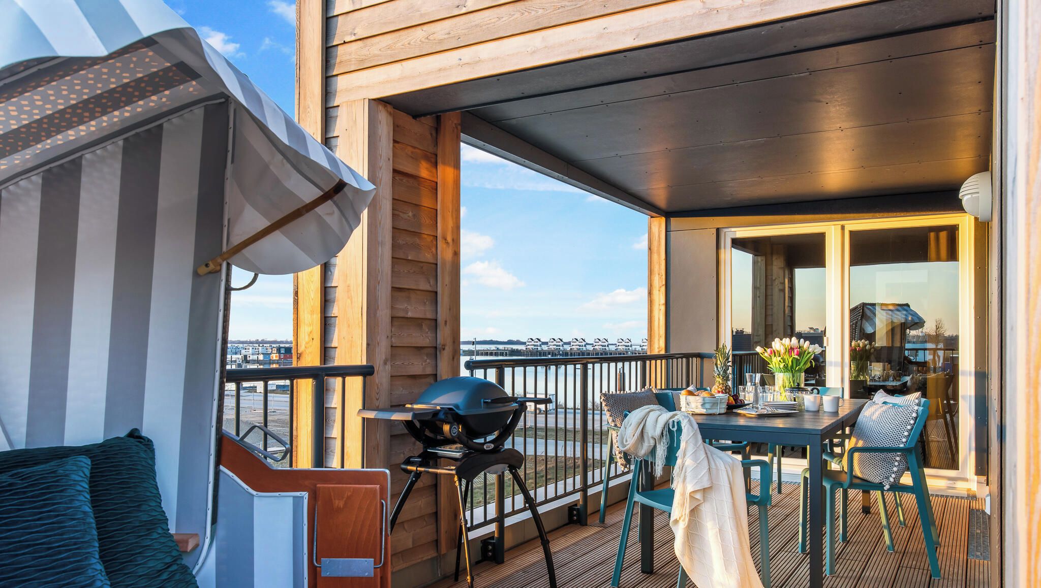 A deck with a table, chairs, a grill, and a view of the water.