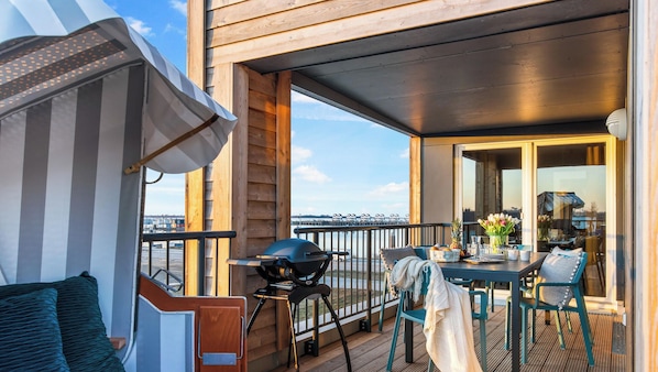 A deck with a table, chairs, a grill, and a view of the water.