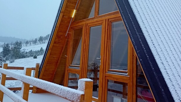 Een houten chalet met grote ramen en een schuin dak, omgeven door sneeuw.