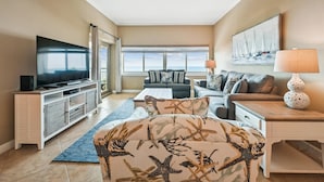A living room with a television, sofa, and coffee table. There is a window with a view of the ocean. - Coastal 5th Floor Ocean Front Views w/ Amenites (Hilton Head Island)