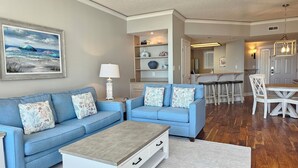 A living room with a blue sofa, a white coffee table, and a painting of a beach scene.