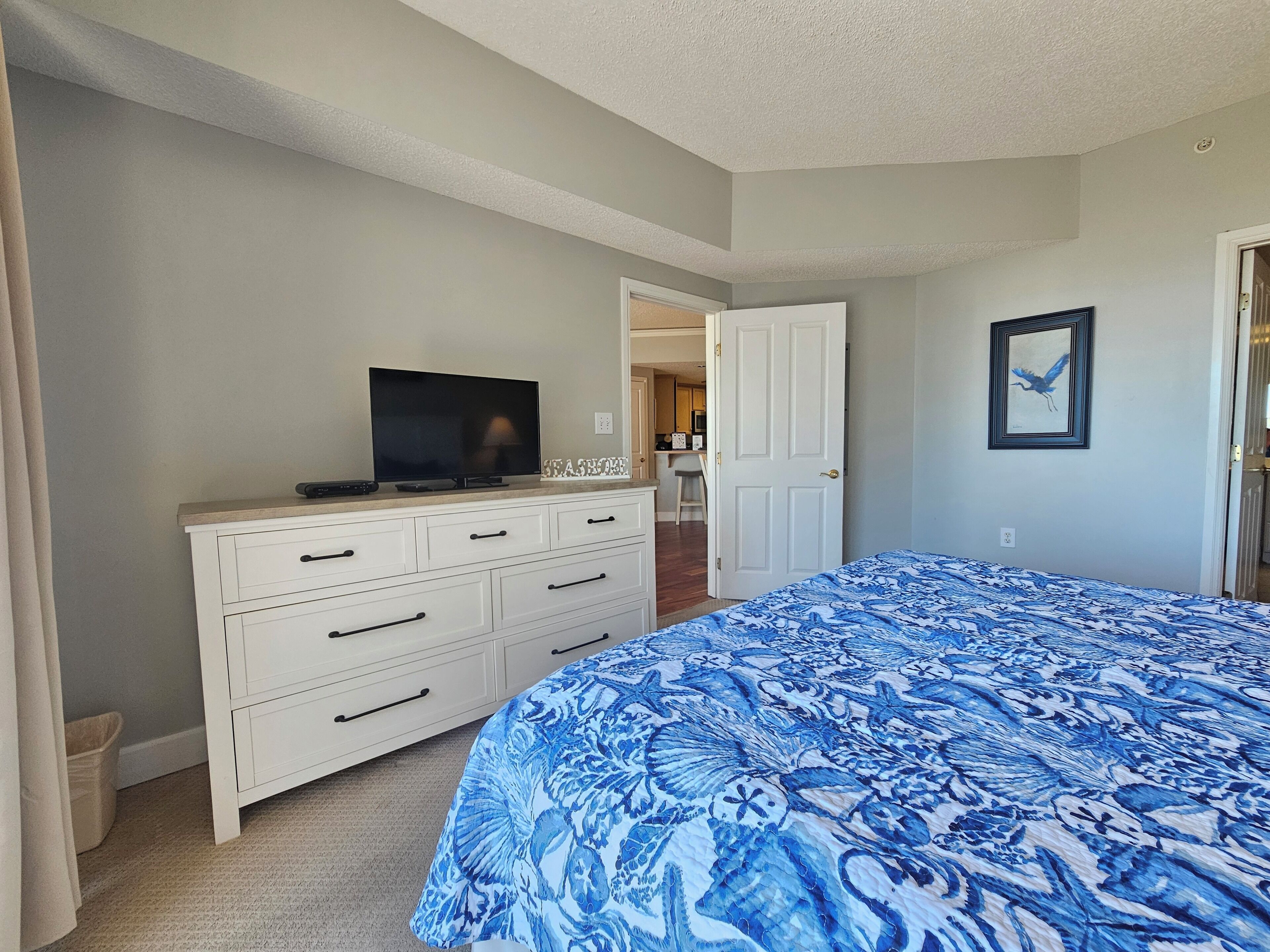 A bedroom with a bed, a dresser, a television, and a door leading to a bathroom.