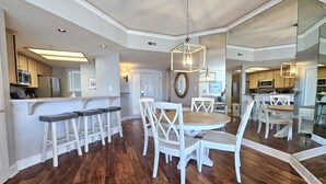 A spacious kitchen with wooden flooring, white bar stools, and a central dining table with white chairs.