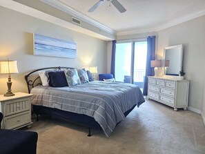 A bedroom with a bed, nightstands, a dresser, a chair, and a large window with curtains.