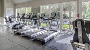 Une salle de sport équipée de plusieurs tapis de course et d’appareils d’exercice, dotée de grandes fenêtres et d’un panneau indiquant la sortie.