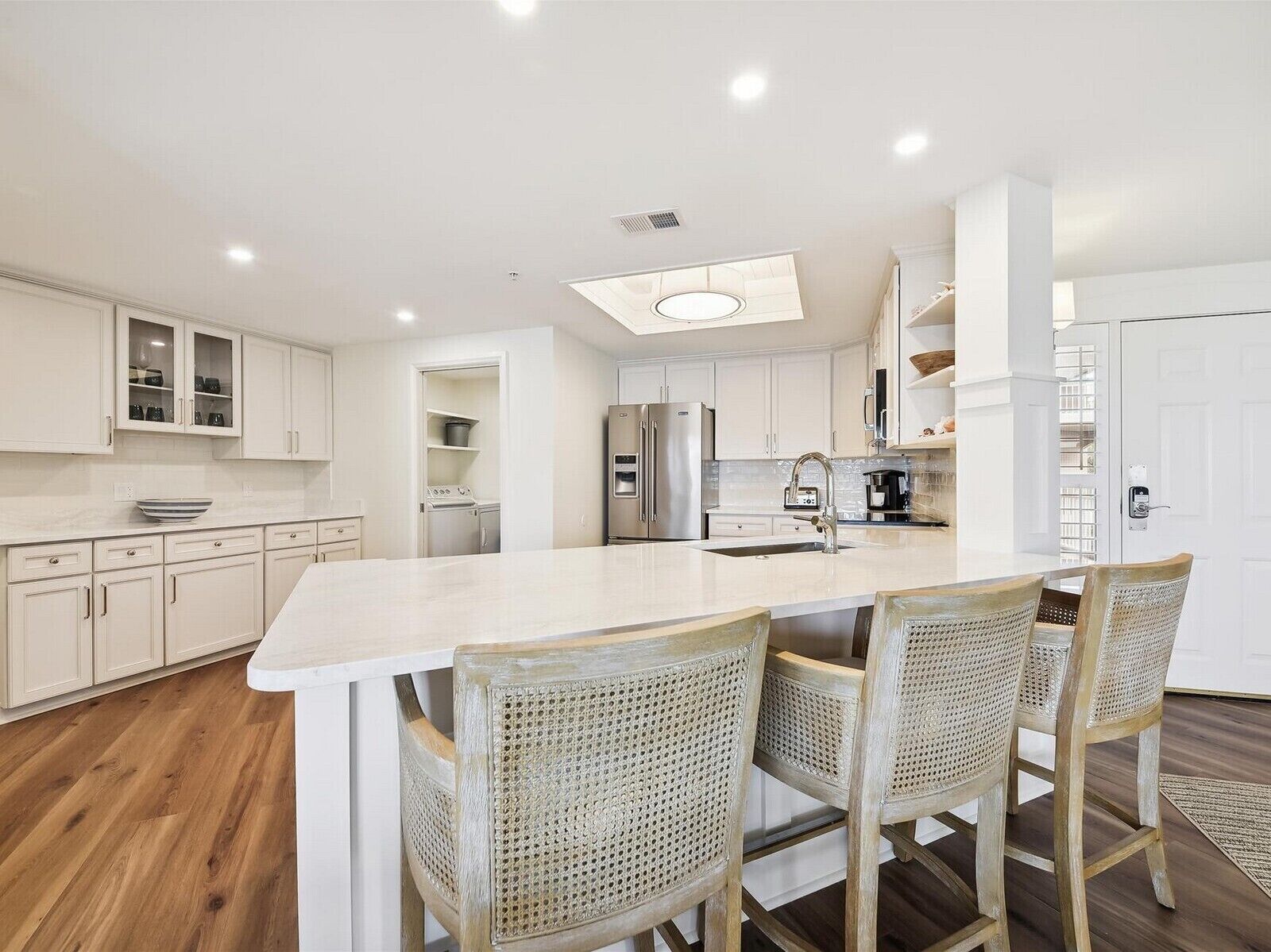 A modern kitchen with white cabinetry, a central island with bar stools, a stainless steel refrigerator, and a built-in oven.