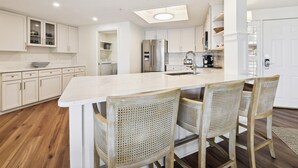 A modern kitchen with white cabinetry, a central island with bar stools, a stainless steel refrigerator, and a built-in oven.