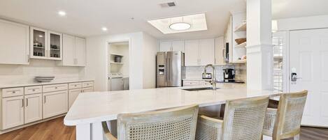 A modern kitchen with white cabinetry, a central island with bar stools, a stainless steel refrigerator, and a built-in oven.