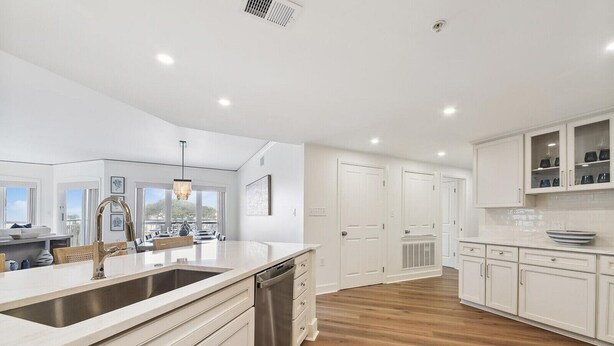 A modern kitchen with white cabinetry, a stainless steel sink, and a wooden floor.