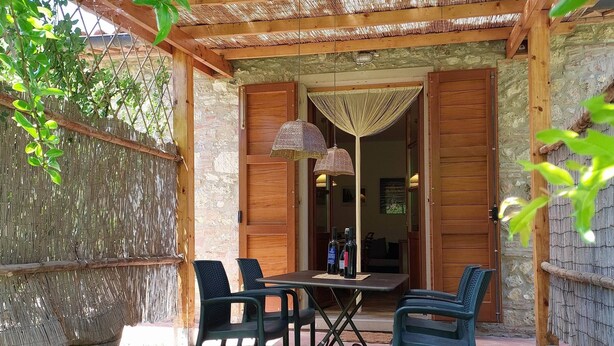 An outdoor patio with a table and chairs, a woven canopy, and a stone wall.