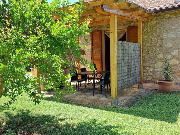 Um edifício de pedra com uma pérgula de madeira e uma mesa com cadeiras no exterior.