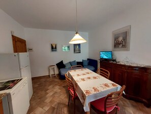 Uma cozinha compacta com geladeira, uma mesa de jantar com cadeiras, um banquinho pequeno e uma televisão em um armário de madeira.