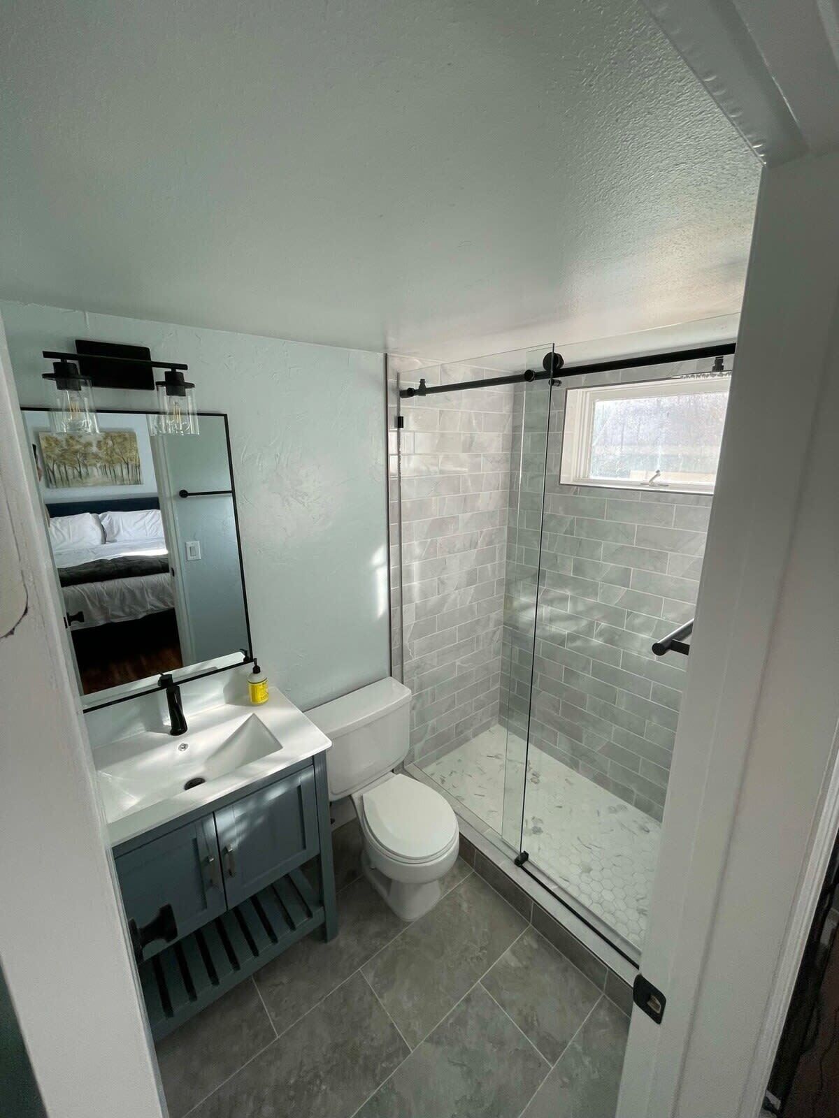 Un baño moderno con cabina de ducha de vidrio, inodoro blanco y tocador con espejo y lavamanos.