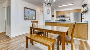 A modern kitchen with wooden cabinets, a central island, and a dining area with a wooden table and bench. - Lovely 2 BDR Condo - Close to Skiing & Main St! (Breckenridge)