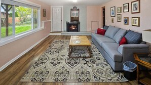 A living room with a fireplace, a sofa, a coffee table, and a rug. - Perch - LFP View Home: Cozy 4BR Home, Lake Washington View Deck, Backyard (Lake Forest Park)