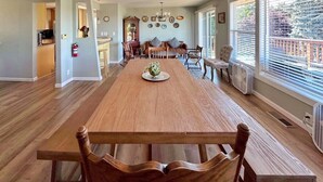 A spacious dining area with a wooden table and chairs, a chandelier, and large windows with blinds. - Perch - LFP View Home: Cozy 4BR Home, Lake Washington View Deck, Backyard (Lake Forest Park)