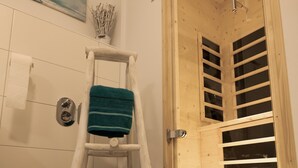 Un baño con recinto de ducha de madera, un perchero blanco y una toalla azul sobre una silla de madera.