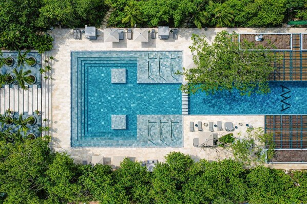 An aerial view of a resort with a central swimming pool, lounge area, and surrounding greenery.