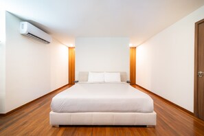 A bedroom with a bed, wooden flooring, a wall-mounted air conditioner, and bedside lamps.