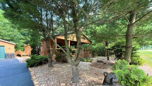 A log cabin with a porch, surrounded by trees and a gravel path.