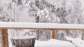 Una terraza de madera con un banco y una silla cubiertos de nieve.