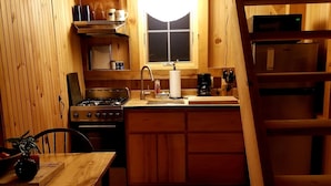 Una cocina acogedora con paredes de madera, una estufa a gas, un lavamanos y una lámpara sobre la encimera.