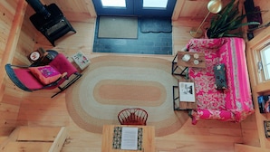 Interior acogedor de una cabaña con piso de madera, una alfombra central, un sofá, un sillón, una mesa con una carta y una chimenea.