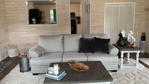 A cozy living room with a grey sofa, a coffee table with books and candles, and a wooden ceiling.