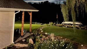 A house with a covered porch, a lawn, and a garden with flowers and a tree.