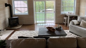 A cozy cabin with a wooden interior, a fireplace, a sofa, a table, and a view of the outdoors through large windows.