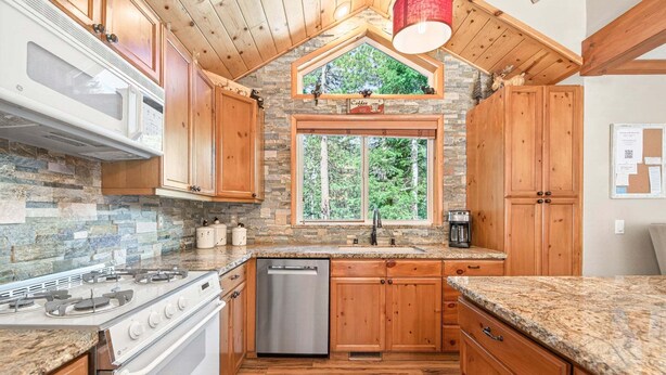 A kitchen with wooden cabinets, a stone backsplash, a built-in microwave, a gas stove, and a dishwasher. - Bear's Lair by Tahoe Getaways - Luxury Cabin w Hot Tub & HOA Access (Truckee)