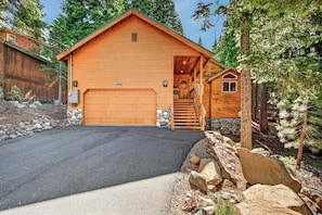 A wooden cabin with a garage, a staircase leading to a porch, and a surrounding natural landscape.