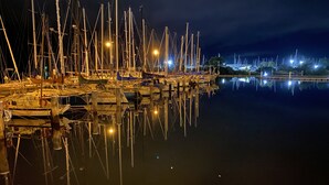 Una marina di notte con imbarcazioni ormeggiate e i loro riflessi visibili sull'acqua.