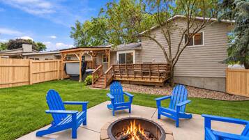 Un jardin avec un foyer, une terrasse en bois et des chaises Adirondack bleues.