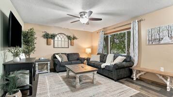A living room with a ceiling fan, two couches, a coffee table, a TV, and a painting on the wall.