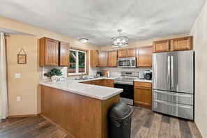 A modern kitchen with wooden cabinets, stainless steel appliances, and a large island. - Family Retreat | Hot Tub, Fire Pit & Game Room (Sioux Falls)
